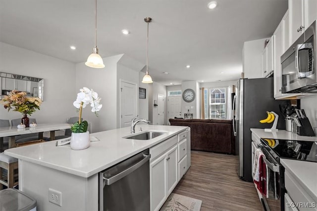 kitchen with a kitchen island with sink, a sink, wood finished floors, appliances with stainless steel finishes, and white cabinets