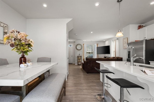 kitchen with a sink, a breakfast bar, wood finished floors, and stainless steel fridge with ice dispenser