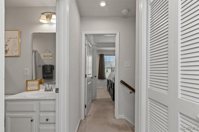 hall featuring light colored carpet, baseboards, and a sink