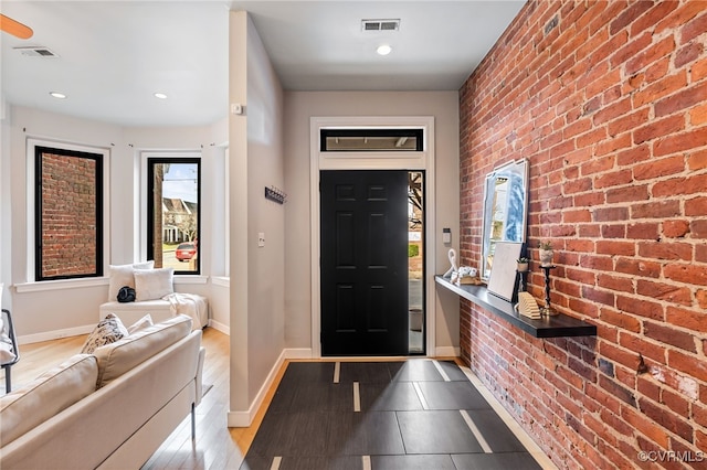 foyer with visible vents, baseboards, and brick wall