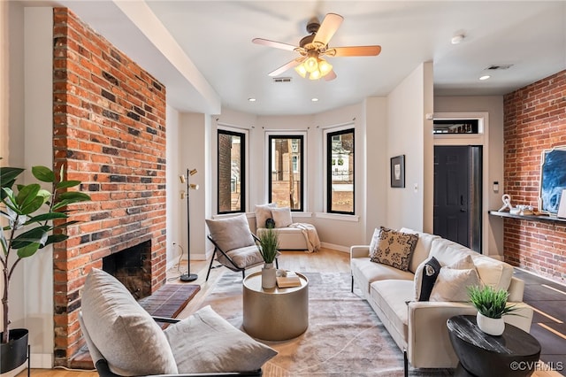 living area with light wood-type flooring, visible vents, a ceiling fan, baseboards, and a brick fireplace