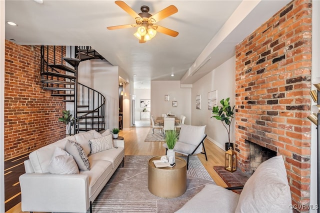 living area with brick wall, baseboards, stairway, a fireplace, and wood finished floors