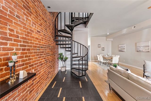 stairs featuring visible vents, wood finished floors, a high ceiling, brick wall, and baseboards