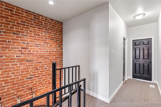 hall featuring an upstairs landing, carpet flooring, brick wall, and baseboards