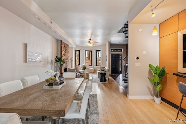 dining space featuring light wood-type flooring, baseboards, a ceiling fan, and stairs