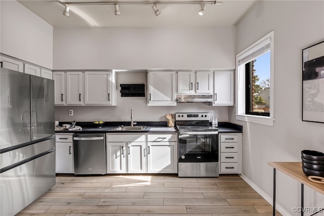 kitchen featuring under cabinet range hood, a sink, dark countertops, stainless steel appliances, and light wood-style floors