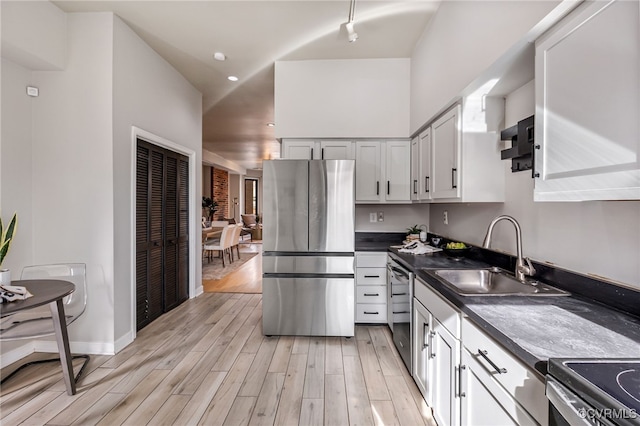 kitchen featuring a sink, dark countertops, range hood, light wood-style floors, and appliances with stainless steel finishes