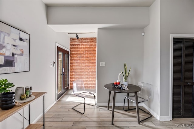 corridor featuring track lighting, brick wall, baseboards, and wood tiled floor