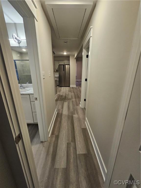 hall featuring a sink, baseboards, attic access, and dark wood-style flooring