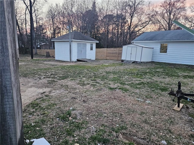 yard at dusk featuring an outdoor structure, a storage unit, and fence