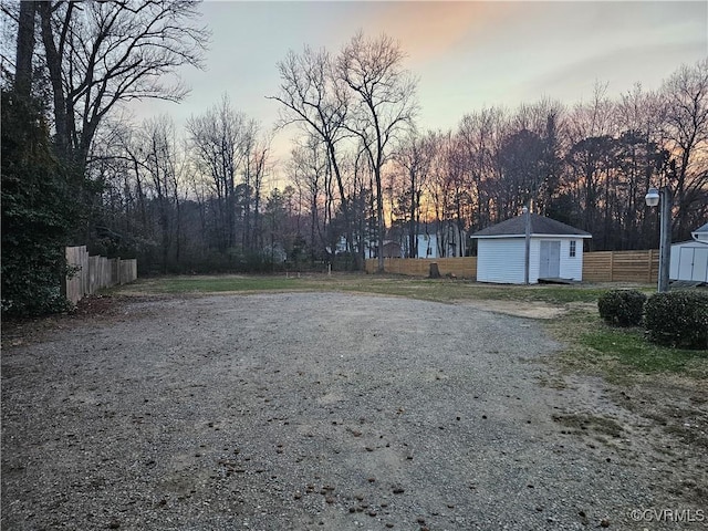 yard at dusk featuring a storage unit, an outdoor structure, and fence