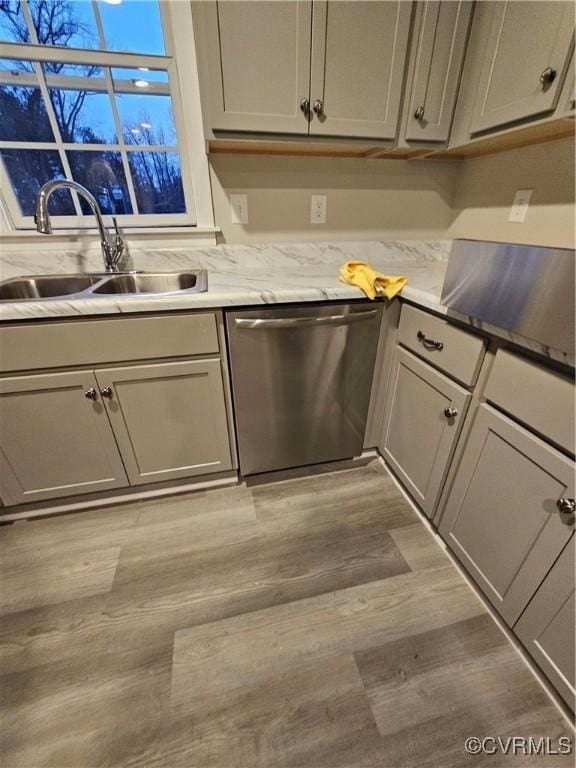 kitchen featuring light wood finished floors, gray cabinets, a sink, light countertops, and dishwasher