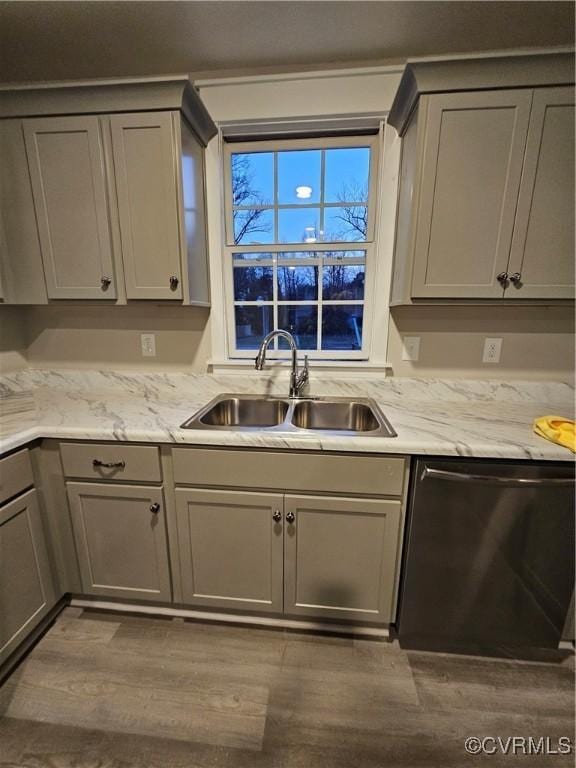 kitchen with gray cabinets, a sink, light stone counters, wood finished floors, and dishwasher