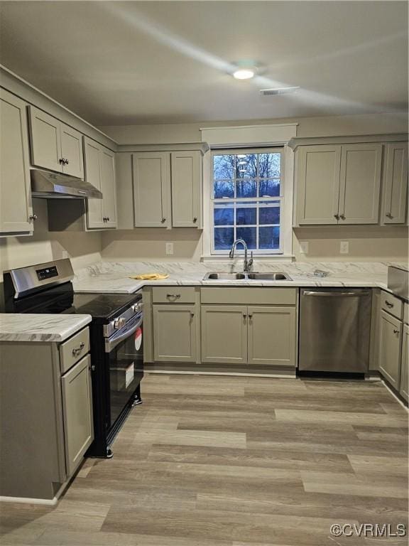 kitchen with gray cabinets, a sink, under cabinet range hood, appliances with stainless steel finishes, and light wood-type flooring