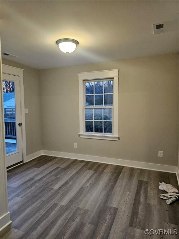 spare room with dark wood finished floors, visible vents, and baseboards