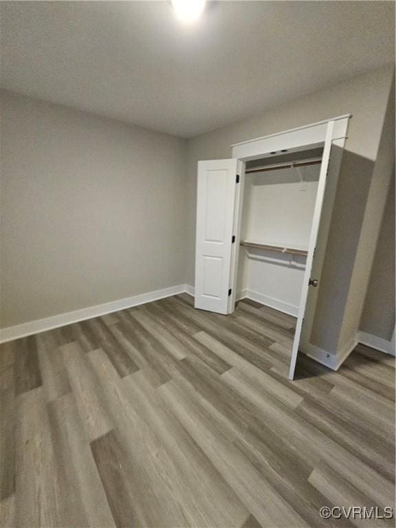 unfurnished bedroom featuring wood finished floors, baseboards, and a closet