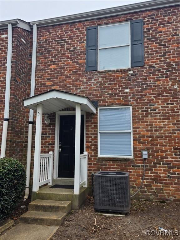 view of exterior entry with central AC unit and brick siding