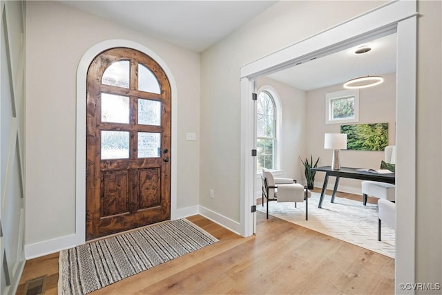 entrance foyer with visible vents, baseboards, arched walkways, and wood finished floors