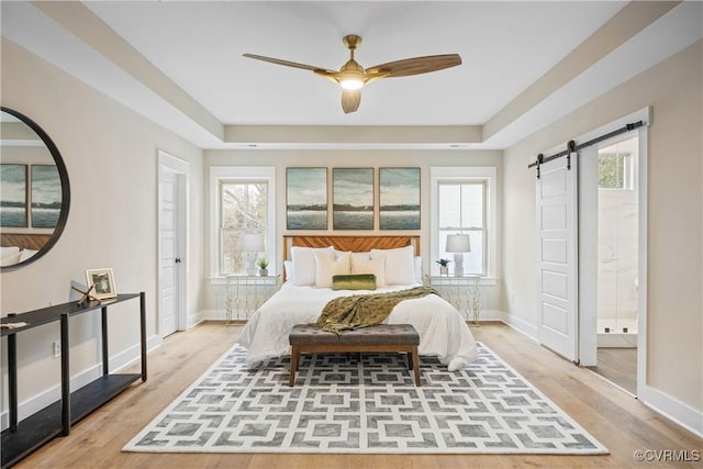 bedroom with multiple windows, baseboards, a barn door, and wood finished floors