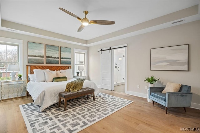 bedroom with baseboards, visible vents, a barn door, light wood-type flooring, and connected bathroom