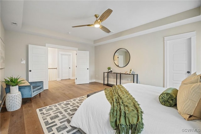 bedroom with a tray ceiling, wood finished floors, visible vents, and baseboards