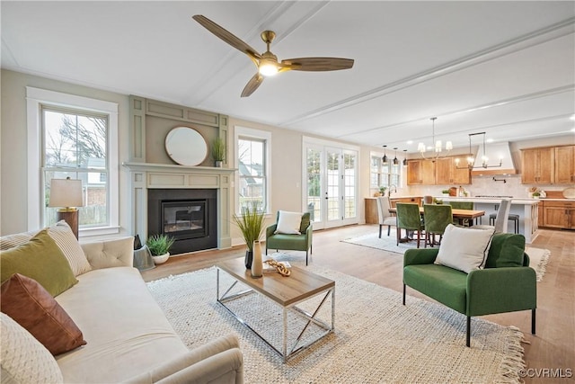 living area with plenty of natural light, ceiling fan with notable chandelier, light wood-type flooring, and a glass covered fireplace