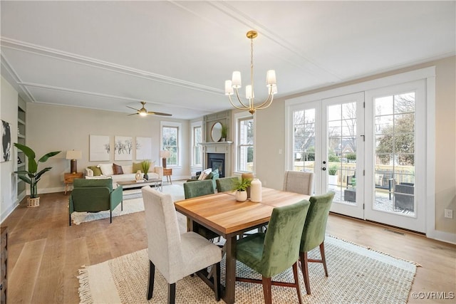 dining area featuring baseboards, light wood finished floors, french doors, a glass covered fireplace, and ceiling fan with notable chandelier