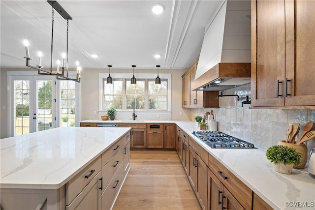 kitchen with tasteful backsplash, stainless steel gas stovetop, light wood finished floors, light stone countertops, and custom exhaust hood