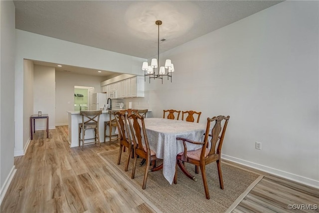 dining space featuring a notable chandelier, baseboards, and light wood finished floors