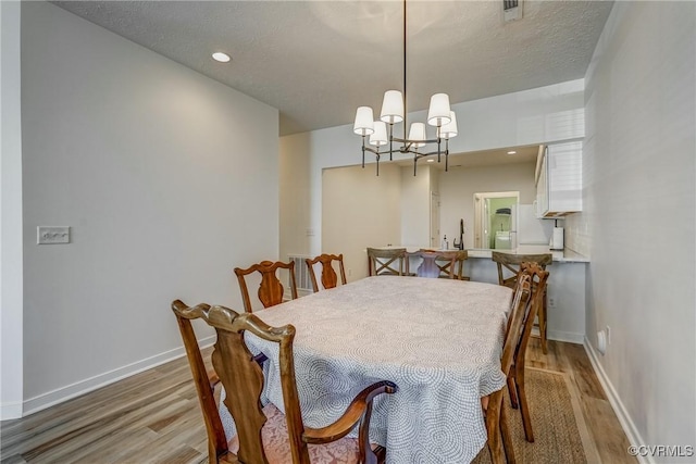 dining space with light wood-type flooring, a textured ceiling, recessed lighting, baseboards, and a chandelier