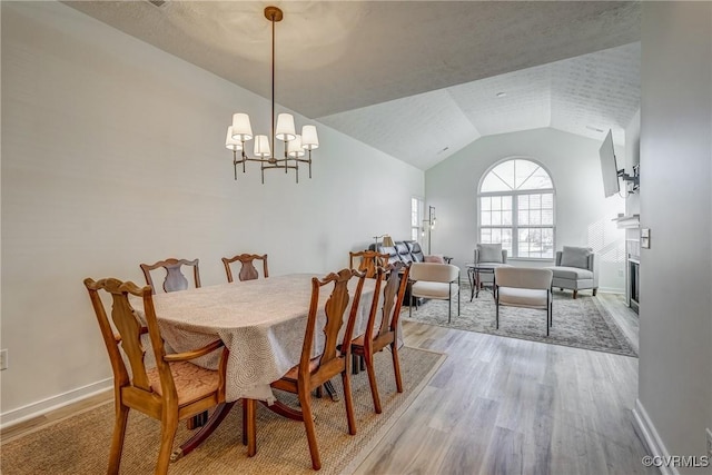 dining space with baseboards, light wood finished floors, high vaulted ceiling, a glass covered fireplace, and a notable chandelier