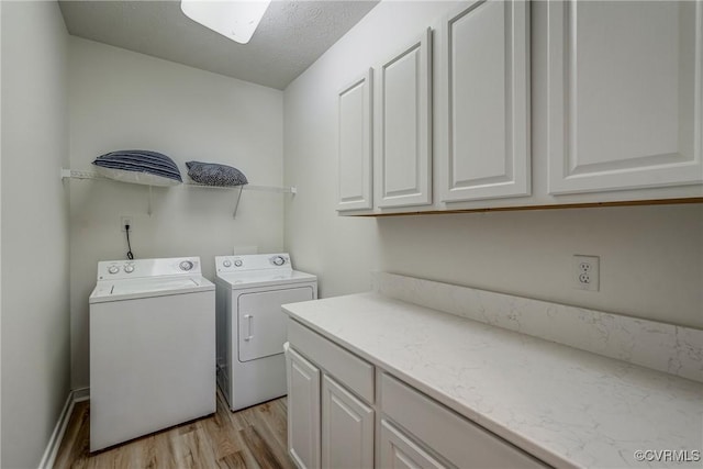 laundry area featuring cabinet space, washing machine and dryer, a textured ceiling, and light wood-style flooring