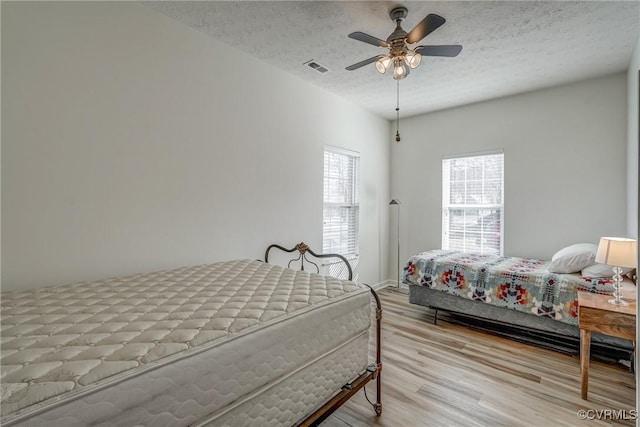 bedroom featuring ceiling fan, visible vents, a textured ceiling, and wood finished floors