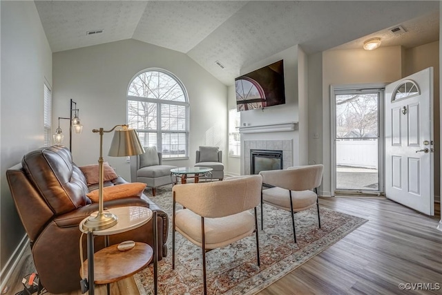 living room with vaulted ceiling, wood finished floors, visible vents, and a tile fireplace