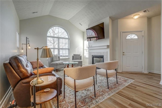 living room with visible vents, light wood-style floors, a fireplace, baseboards, and vaulted ceiling