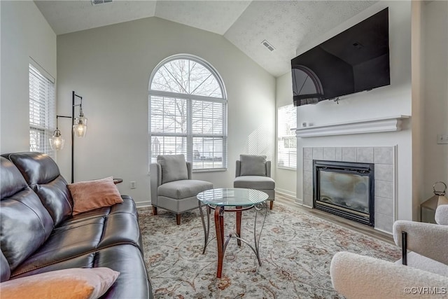 living area with visible vents, plenty of natural light, lofted ceiling, and a tiled fireplace