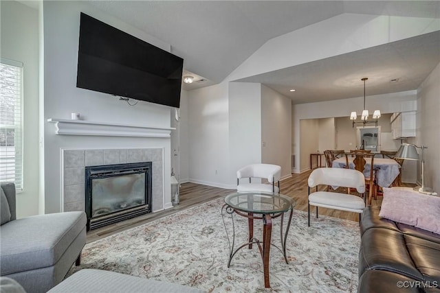 living area featuring wood finished floors, baseboards, an inviting chandelier, lofted ceiling, and a tile fireplace