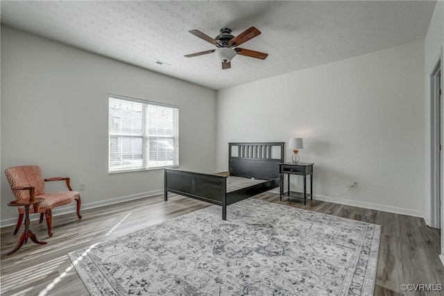 bedroom featuring visible vents, a textured ceiling, baseboards, and wood finished floors