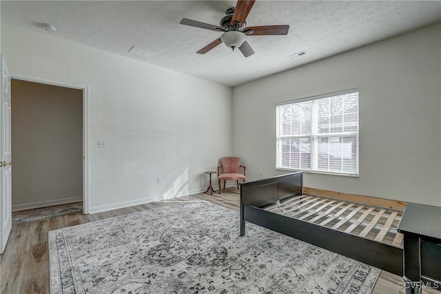 bedroom featuring visible vents, baseboards, a textured ceiling, and wood finished floors