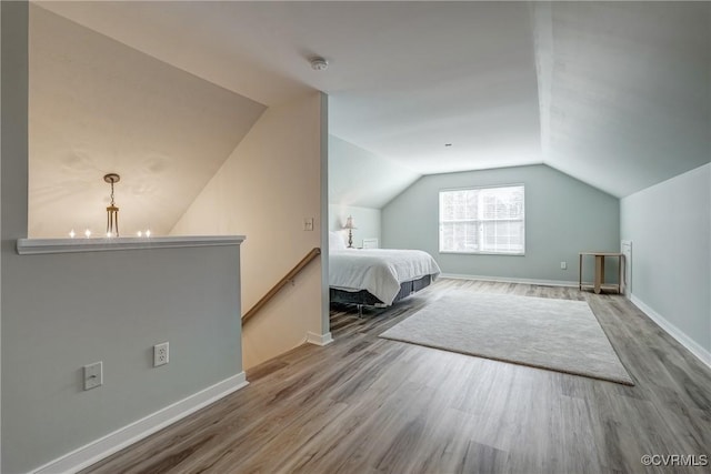 unfurnished bedroom with a notable chandelier, baseboards, lofted ceiling, and wood finished floors