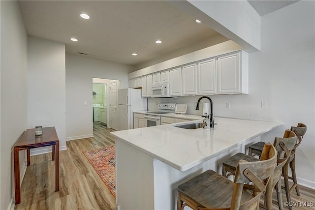 kitchen featuring washer and clothes dryer, a breakfast bar area, light countertops, white appliances, and a sink