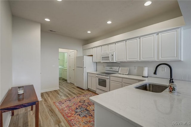 kitchen with white appliances, washing machine and clothes dryer, a sink, white cabinetry, and light wood-type flooring