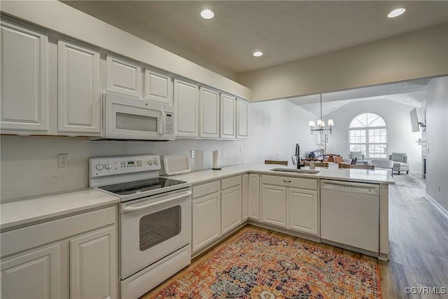 kitchen with a sink, open floor plan, white appliances, a peninsula, and an inviting chandelier