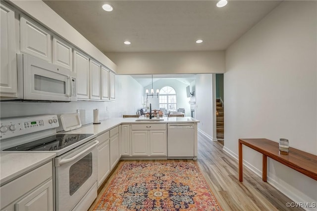 kitchen featuring white appliances, a peninsula, light wood-style flooring, a sink, and light countertops