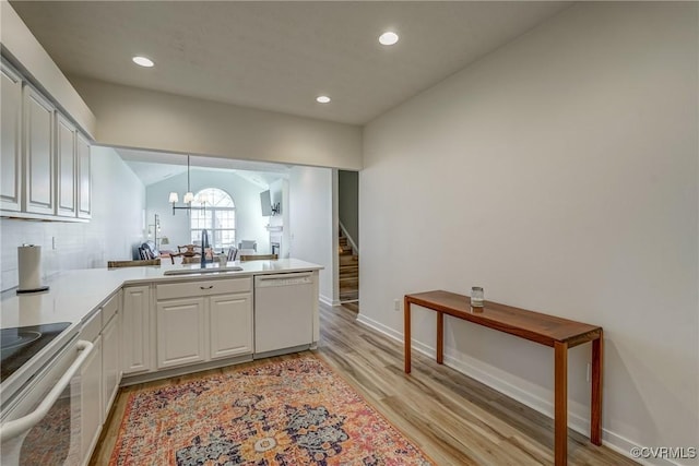 kitchen featuring light wood finished floors, a peninsula, white dishwasher, a sink, and light countertops