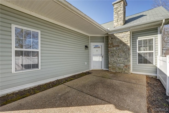 doorway to property with stone siding, a patio, a chimney, and a shingled roof