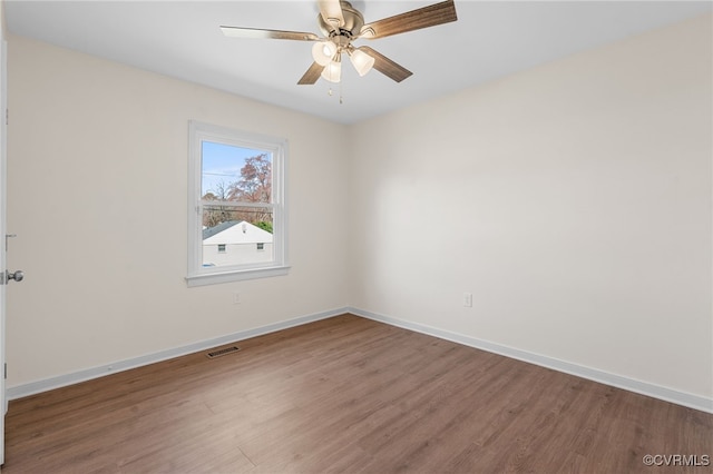 spare room with a ceiling fan, visible vents, wood finished floors, and baseboards