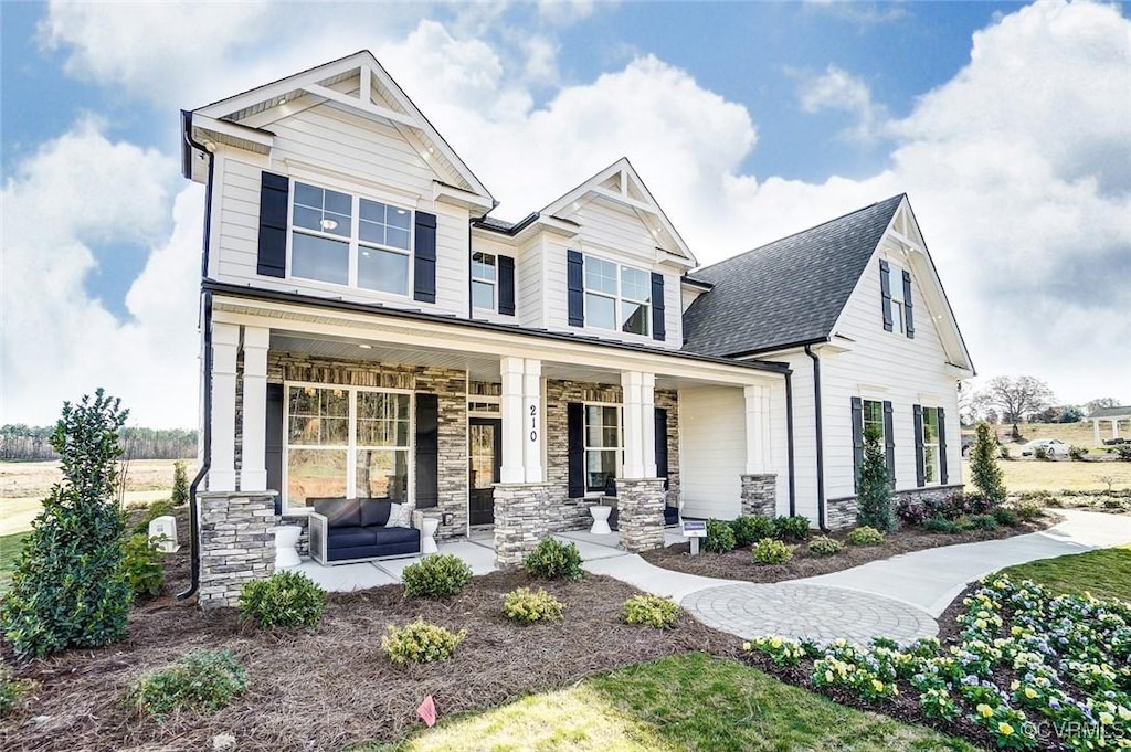 craftsman-style home with covered porch, stone siding, and a shingled roof