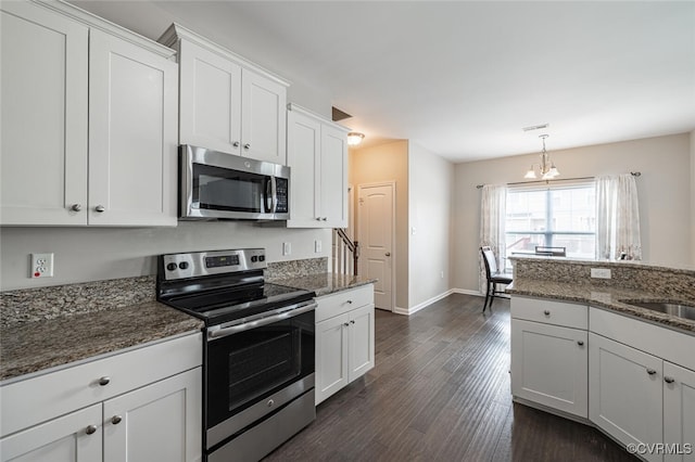 kitchen featuring a notable chandelier, white cabinetry, dark stone counters, appliances with stainless steel finishes, and dark wood-style flooring