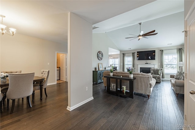 living room with ceiling fan with notable chandelier, dark wood-style floors, a fireplace, baseboards, and vaulted ceiling